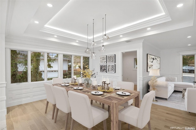 dining space with light hardwood / wood-style floors, a raised ceiling, and plenty of natural light