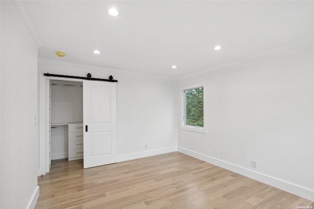 unfurnished room with a barn door, light wood-type flooring, and crown molding