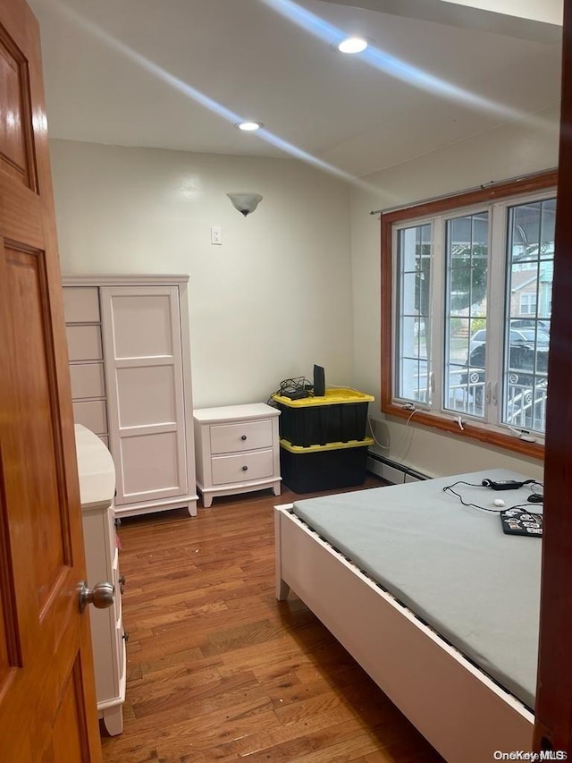 bedroom with light hardwood / wood-style floors and a baseboard heating unit