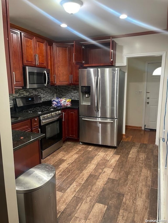 kitchen featuring backsplash, dark stone countertops, stainless steel appliances, and dark wood-type flooring