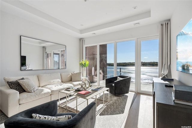 living room featuring a water view, plenty of natural light, hardwood / wood-style flooring, and a tray ceiling