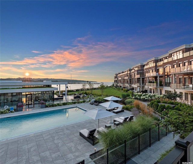 pool at dusk featuring a water view and a patio