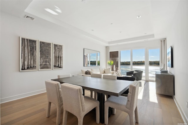 dining room with a raised ceiling, a water view, and light wood-type flooring