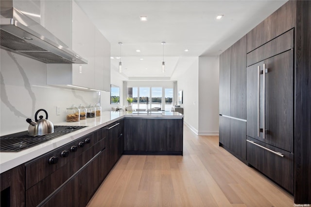 kitchen with wall chimney exhaust hood, stainless steel gas cooktop, pendant lighting, white cabinets, and light hardwood / wood-style floors