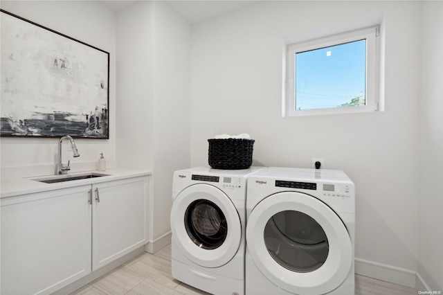 clothes washing area with washer and clothes dryer, cabinets, and sink