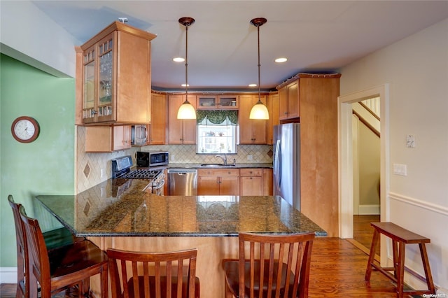 kitchen with sink, dark hardwood / wood-style floors, dark stone countertops, appliances with stainless steel finishes, and kitchen peninsula