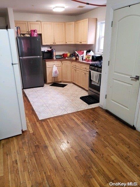 kitchen with light brown cabinets, black appliances, and light wood-type flooring