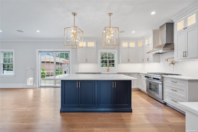 kitchen with pendant lighting, white cabinets, wall chimney exhaust hood, light wood-type flooring, and high end stove