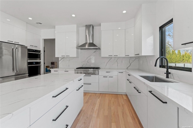 kitchen featuring white cabinets, sink, wall chimney exhaust hood, light wood-type flooring, and appliances with stainless steel finishes