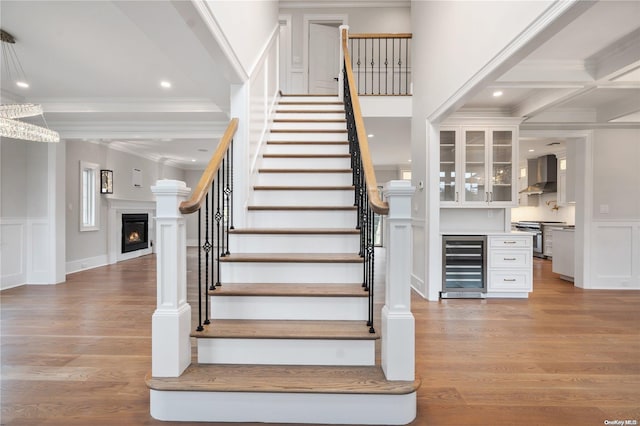 stairway with hardwood / wood-style floors, beverage cooler, ornamental molding, and beam ceiling