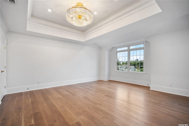 empty room with a raised ceiling, crown molding, a chandelier, and hardwood / wood-style flooring