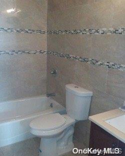 full bathroom featuring vanity, toilet, tile walls, and tiled shower / bath combo