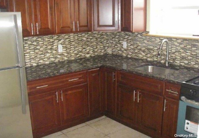 kitchen with decorative backsplash, white appliances, sink, light tile patterned floors, and dark stone countertops