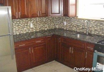 kitchen featuring dark stone counters, white refrigerator, sink, decorative backsplash, and light tile patterned floors