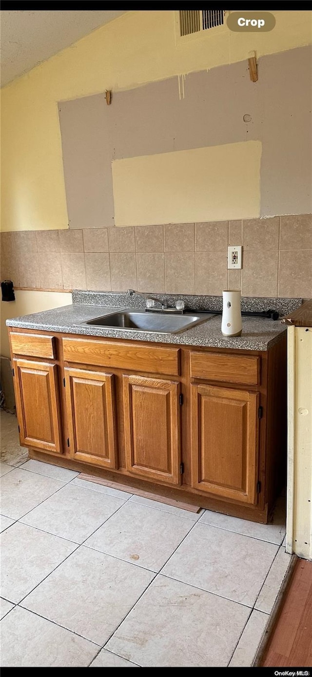 kitchen featuring tasteful backsplash, sink, light tile patterned floors, and lofted ceiling