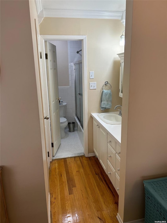 full bathroom featuring vanity, crown molding, shower / bath combination with glass door, hardwood / wood-style flooring, and toilet