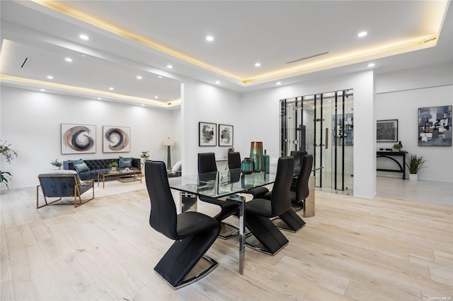 dining area with light wood-type flooring and a raised ceiling