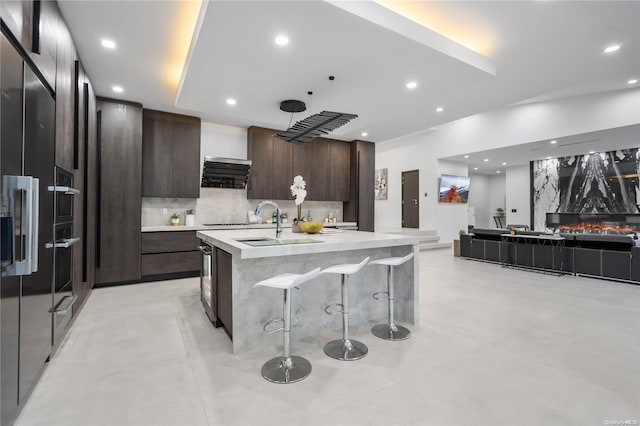 kitchen with backsplash, dark brown cabinetry, a kitchen island with sink, and a kitchen bar