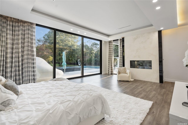 bedroom with hardwood / wood-style floors, access to outside, expansive windows, a raised ceiling, and a premium fireplace