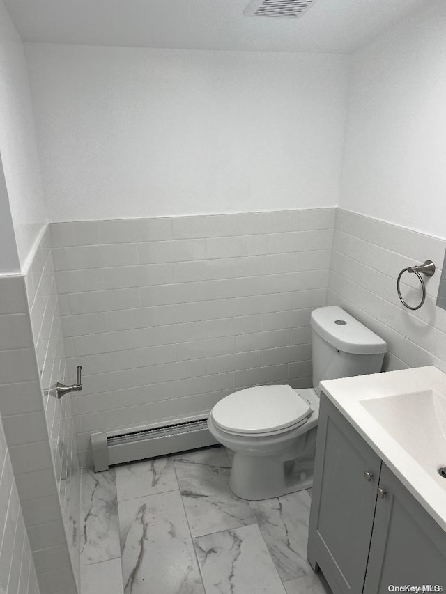 bathroom with vanity, toilet, baseboard heating, and tile walls