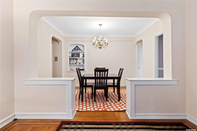 dining room featuring crown molding, built in features, wood-type flooring, and an inviting chandelier