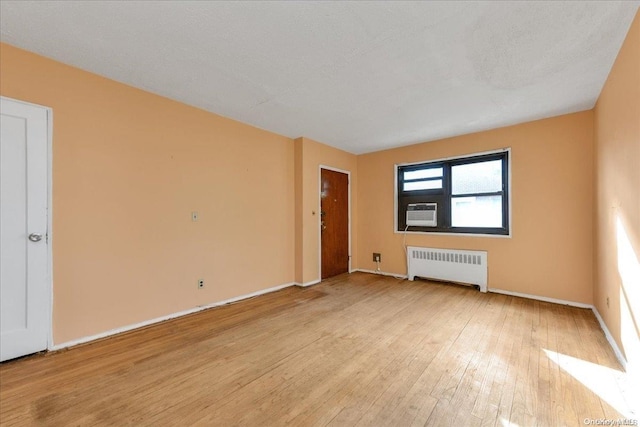 unfurnished room featuring cooling unit, radiator heating unit, a textured ceiling, and light hardwood / wood-style flooring