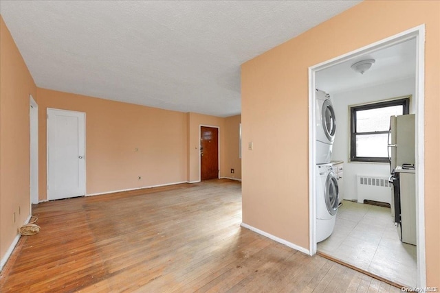 laundry room featuring radiator heating unit, a textured ceiling, stacked washing maching and dryer, and light hardwood / wood-style floors