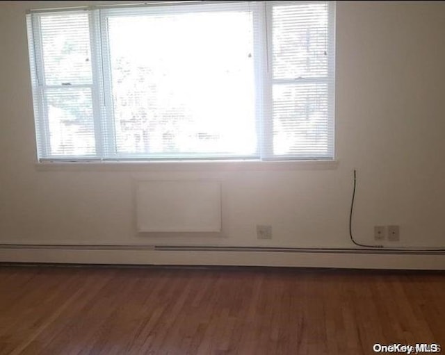 spare room with a healthy amount of sunlight, dark wood-type flooring, and a baseboard heating unit