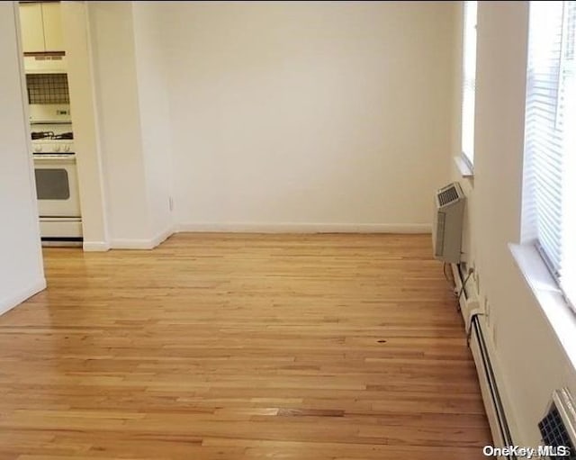 unfurnished room with a baseboard radiator, light hardwood / wood-style floors, and a wall mounted air conditioner