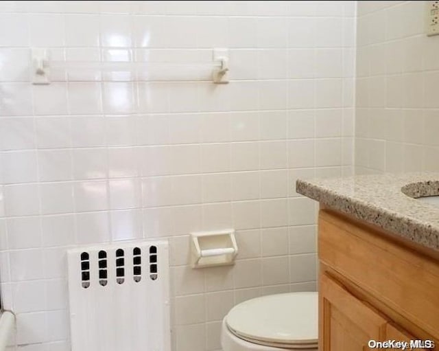 bathroom featuring radiator heating unit, vanity, tile walls, and toilet