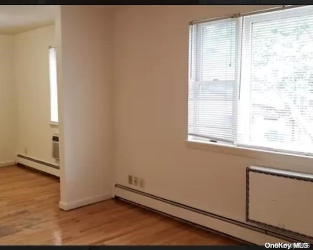 empty room with light hardwood / wood-style floors, a wealth of natural light, and a baseboard heating unit