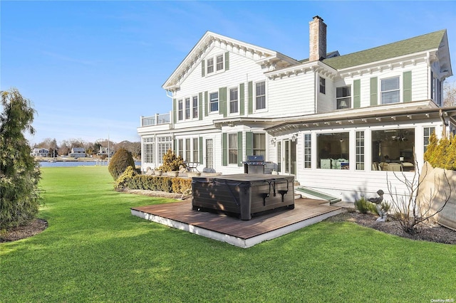 back of property with a wooden deck, a yard, and a hot tub