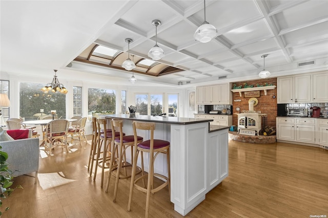 kitchen with coffered ceiling, ceiling fan with notable chandelier, pendant lighting, light hardwood / wood-style flooring, and a kitchen island