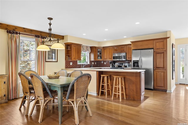 kitchen with decorative backsplash, appliances with stainless steel finishes, light wood-type flooring, and decorative light fixtures