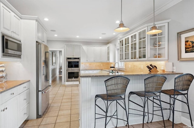 kitchen with kitchen peninsula, appliances with stainless steel finishes, white cabinets, and light stone counters