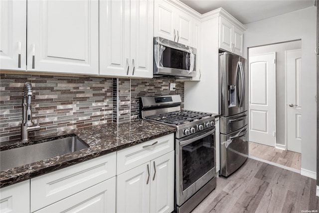 kitchen with white cabinetry, sink, dark stone countertops, light hardwood / wood-style floors, and appliances with stainless steel finishes