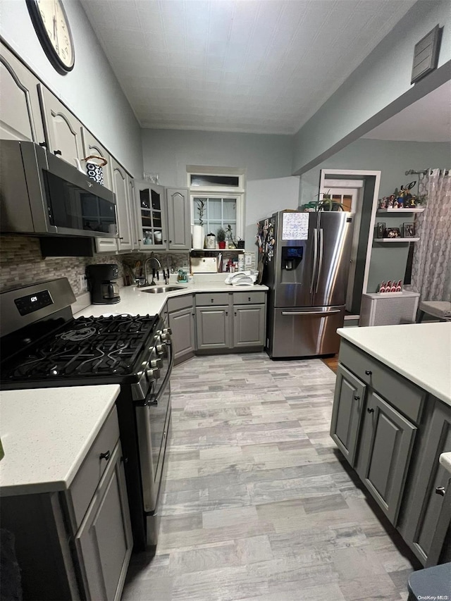 kitchen with appliances with stainless steel finishes, tasteful backsplash, gray cabinetry, sink, and light hardwood / wood-style flooring