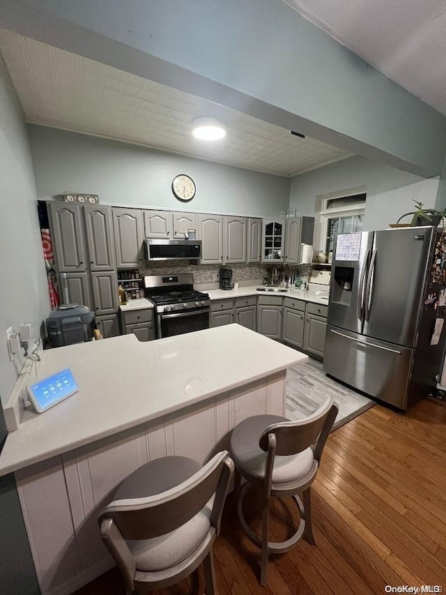 kitchen featuring kitchen peninsula, appliances with stainless steel finishes, light wood-type flooring, tasteful backsplash, and gray cabinetry