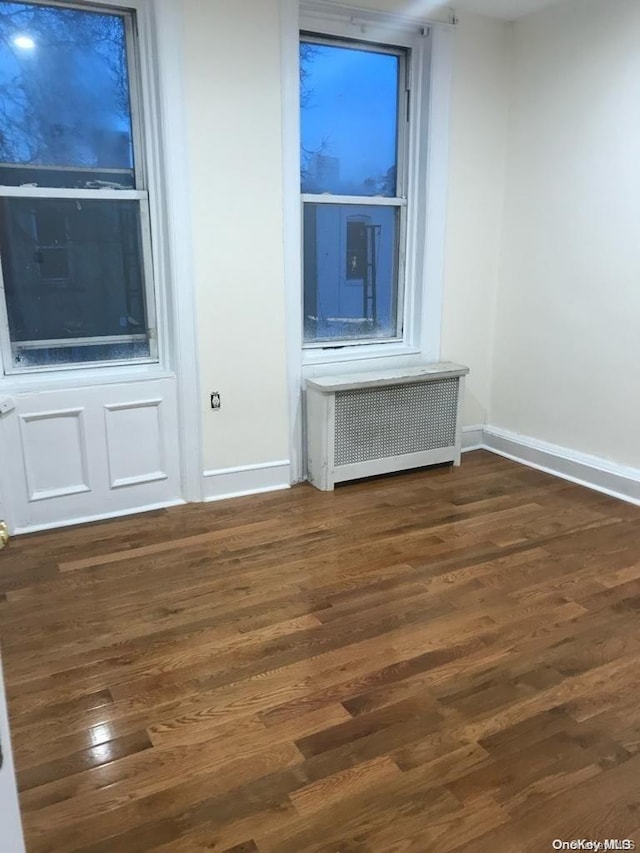 unfurnished room featuring radiator heating unit and dark hardwood / wood-style floors