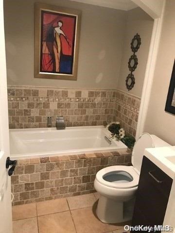 bathroom featuring tiled tub, tile patterned flooring, vanity, and toilet