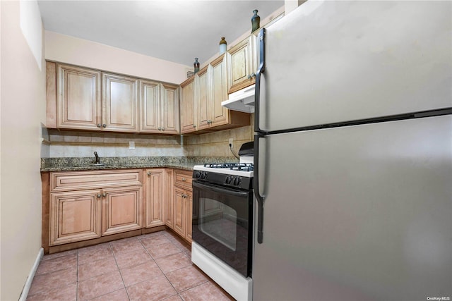 kitchen featuring decorative backsplash, stainless steel fridge, white gas range, dark stone countertops, and light tile patterned flooring