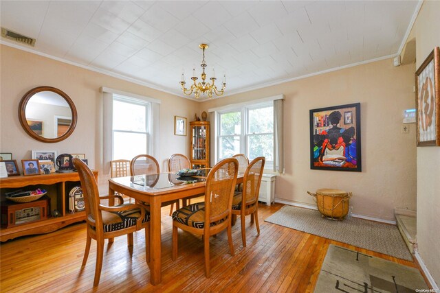 dining space with a wealth of natural light, wood-type flooring, a notable chandelier, and ornamental molding