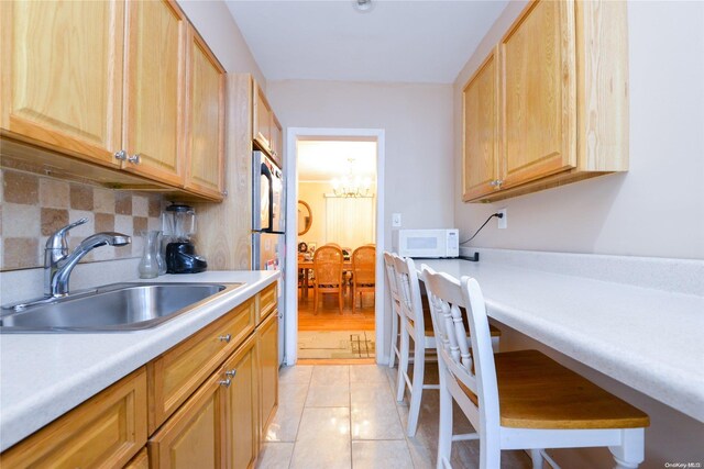 kitchen with tasteful backsplash, sink, light tile patterned floors, a notable chandelier, and stainless steel refrigerator