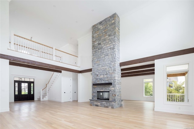 unfurnished living room with a stone fireplace, beamed ceiling, a towering ceiling, and light hardwood / wood-style floors