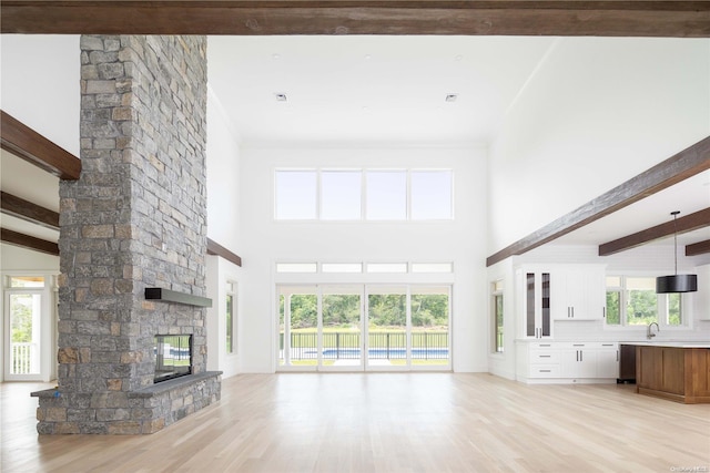 unfurnished living room with beam ceiling, light hardwood / wood-style floors, a fireplace, and a wealth of natural light