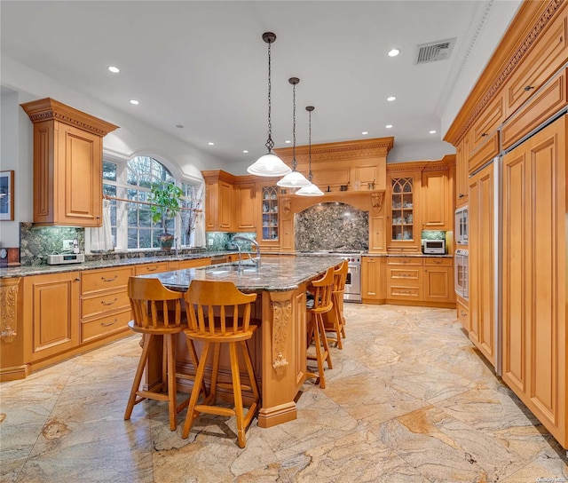 kitchen featuring a kitchen bar, decorative backsplash, a kitchen island with sink, and light stone countertops