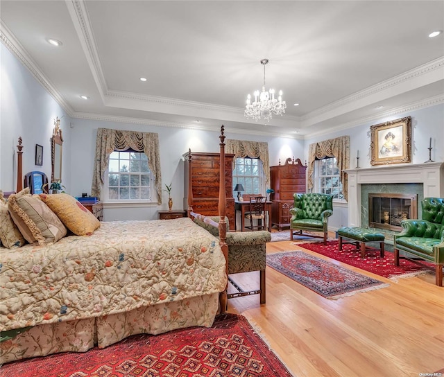 bedroom with a raised ceiling, crown molding, hardwood / wood-style flooring, a premium fireplace, and a notable chandelier