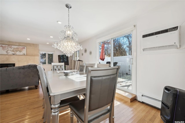 dining room with a tile fireplace, a baseboard radiator, a wall mounted air conditioner, a chandelier, and light wood-type flooring