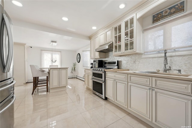 kitchen with cream cabinets, a kitchen breakfast bar, sink, decorative backsplash, and stainless steel appliances