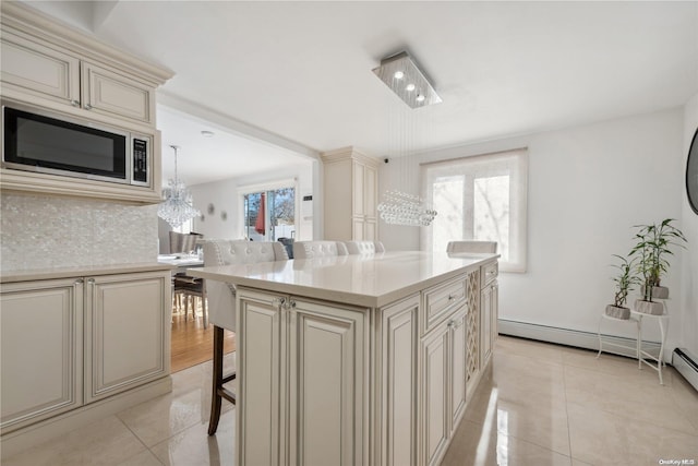 kitchen featuring a center island, stainless steel microwave, light tile patterned floors, cream cabinetry, and a kitchen bar